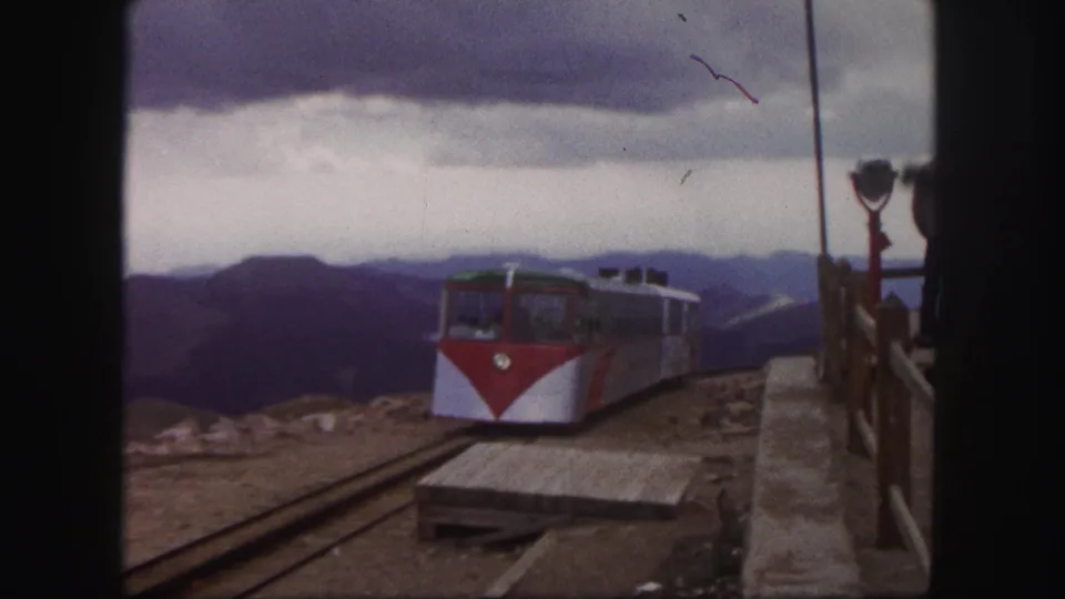 1958 Colorado Springs frame showing the railcar farther from the camera on station tracks, with platform boards and mountains visible.