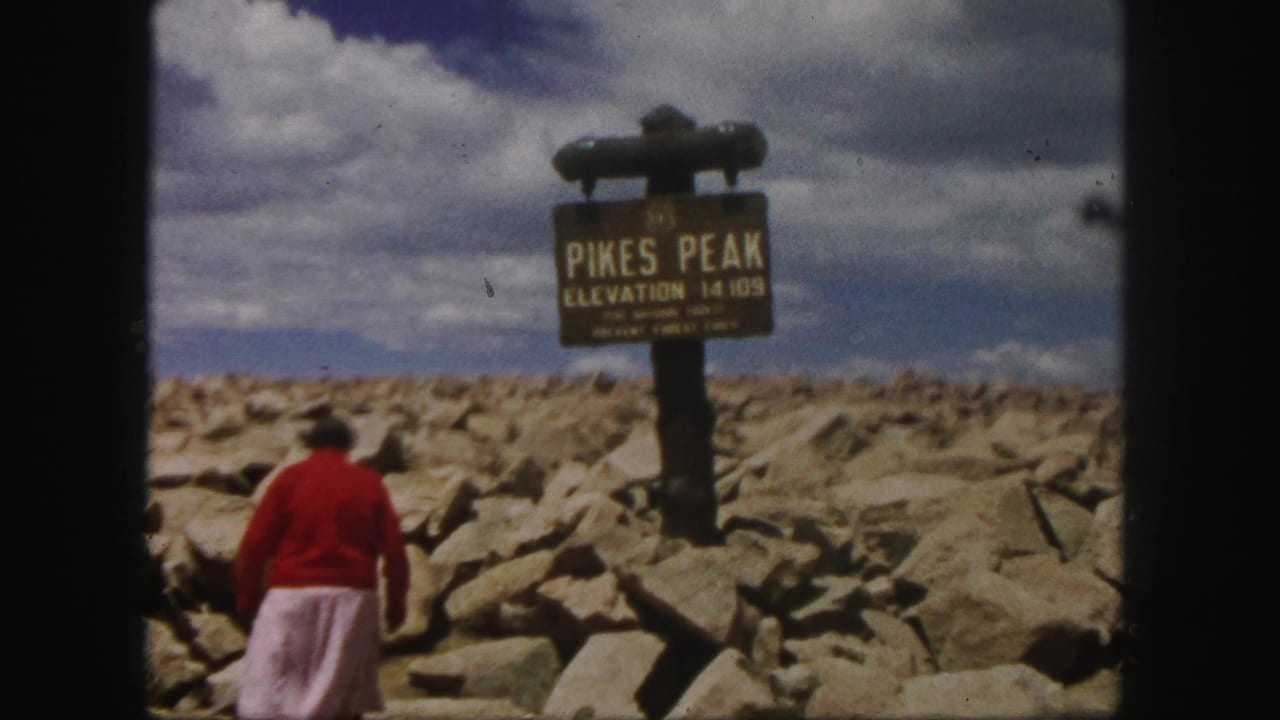 Woman in a red sweater walks over rocks toward a Pikes Peak elevation sign.