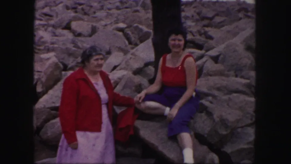 Two adult women pose on rocky ground near the Pikes Peak signpost in a 1958 Colorado home-movie frame.