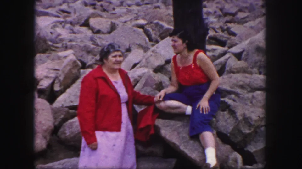 This Colorado Springs 1958 frame shows the women interacting naturally on rocks, with the seated woman turned toward the standing woman in a red jacket.