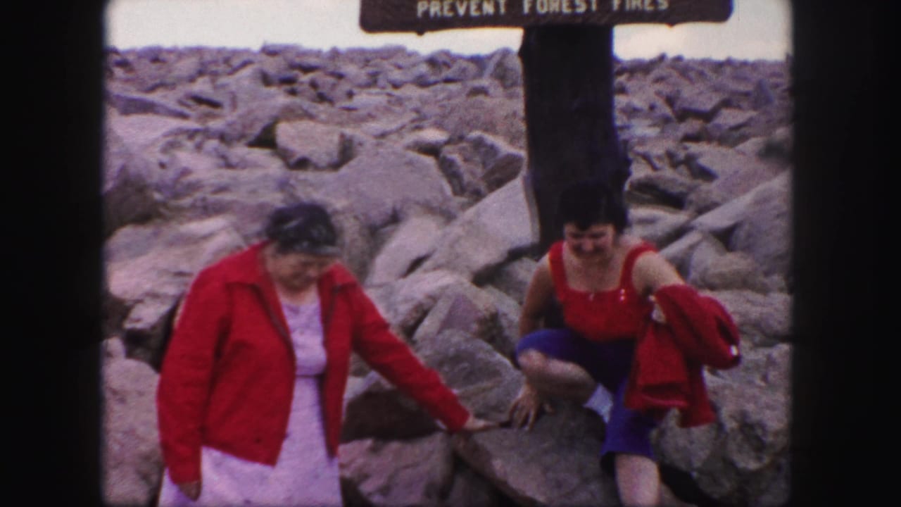 Two women in red clothing move across rocky ground below a fire-prevention sign.