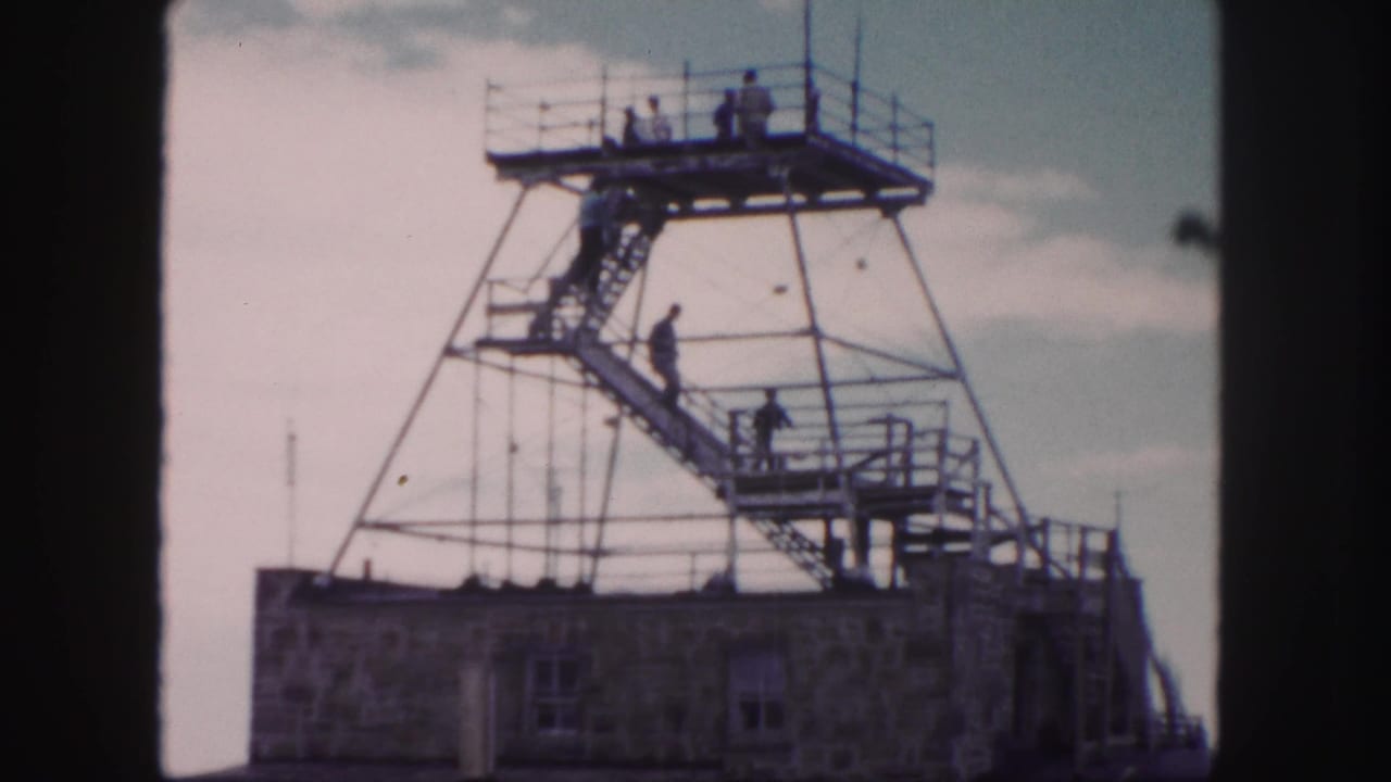 Visitors on a metal observation tower above a stone building.