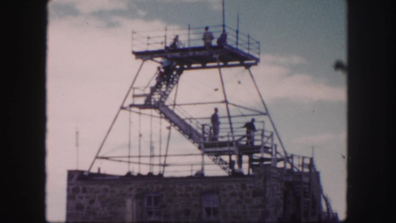 People gather on an elevated metal platform above a stone structure.