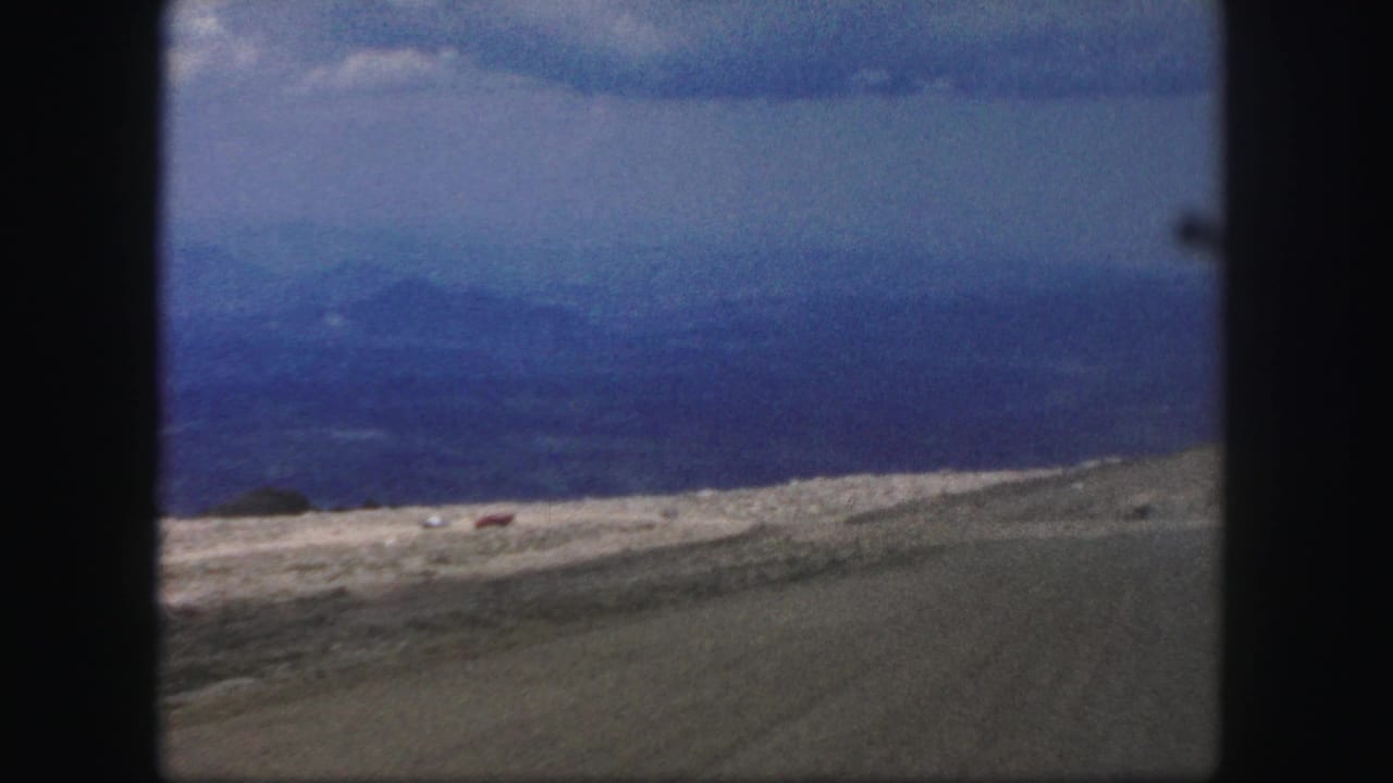 1958 8mm view near Colorado Springs showing arid hills, a pale road, distant blue mountains, and dark window-like framing.