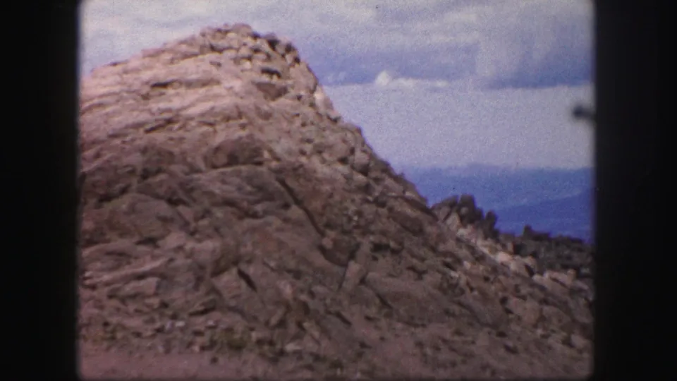 A rocky outcrop near Colorado Springs fills the 1958 8mm frame, with cloudy sky and distant blue ridges behind it.