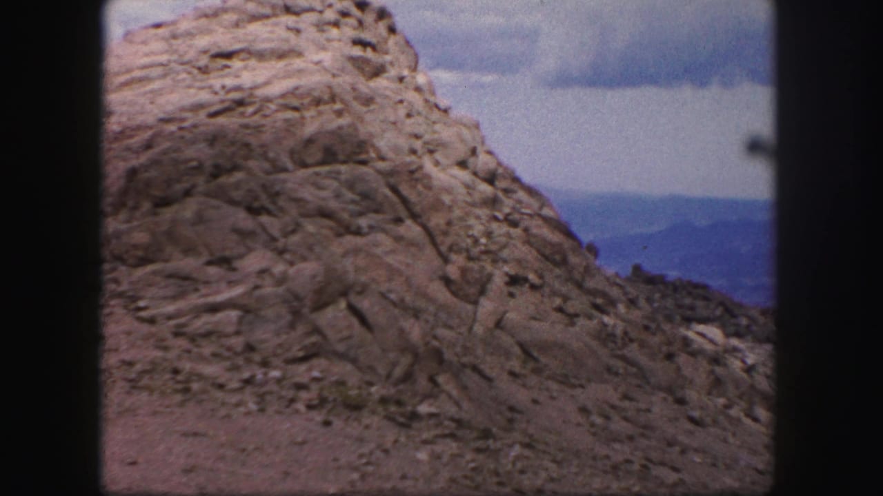Large rounded rock formation with scattered stones and blue hills in the background.