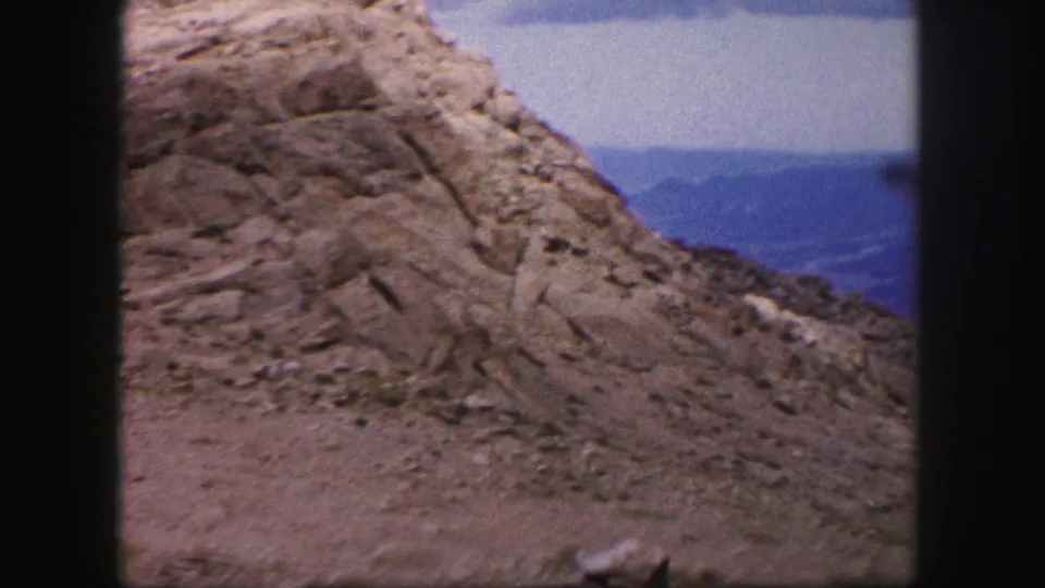 1958 Colorado Springs home-movie view of a rocky slope, eroded stone textures, distant valley, and cloudy mountain sky.