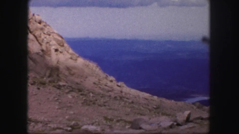 1950s 8mm frame of rough rock and a sloped mountain edge looking out over blue distant terrain near Colorado Springs.