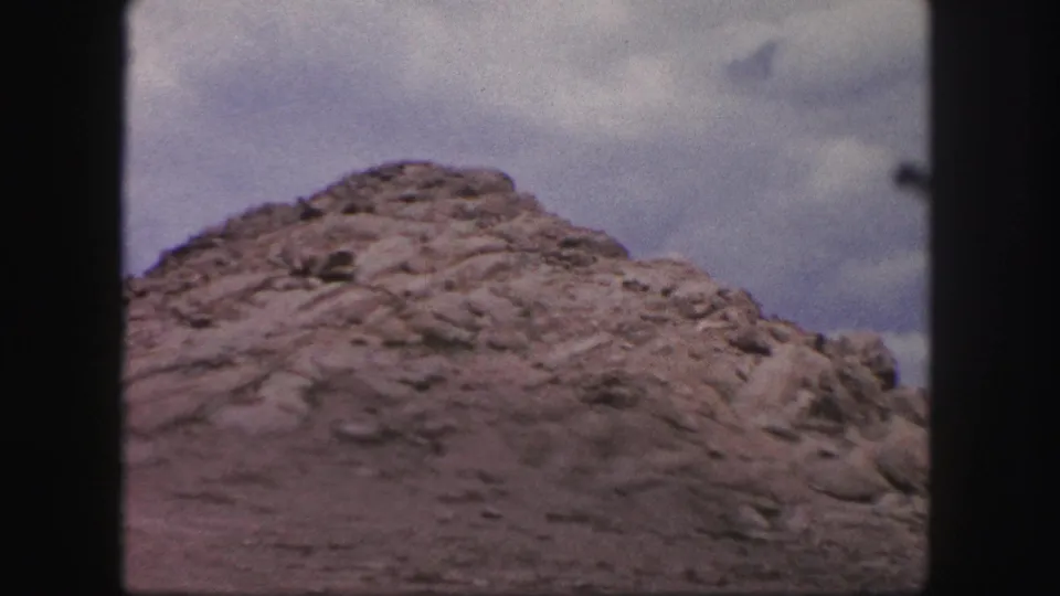 Home-movie frame from the Colorado Springs mountain view, centered on a rounded rocky mound beneath a bright clouded sky.