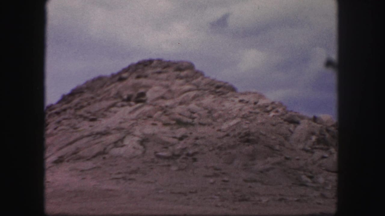 Rock mound and cloudy sky framed by dark vertical window borders.