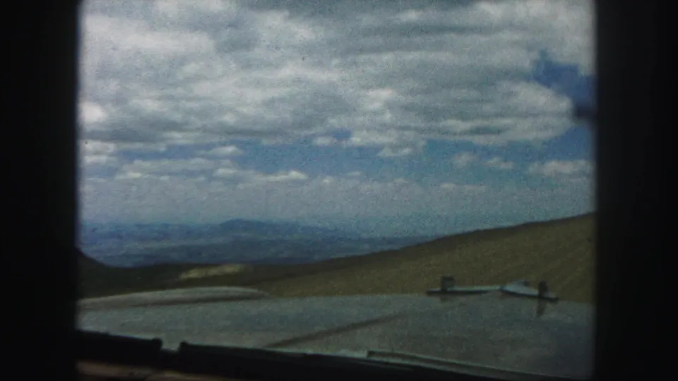 In-car 8mm view in the Colorado Springs area, with the vehicle edge below rolling hills and a wide sky of broken clouds.