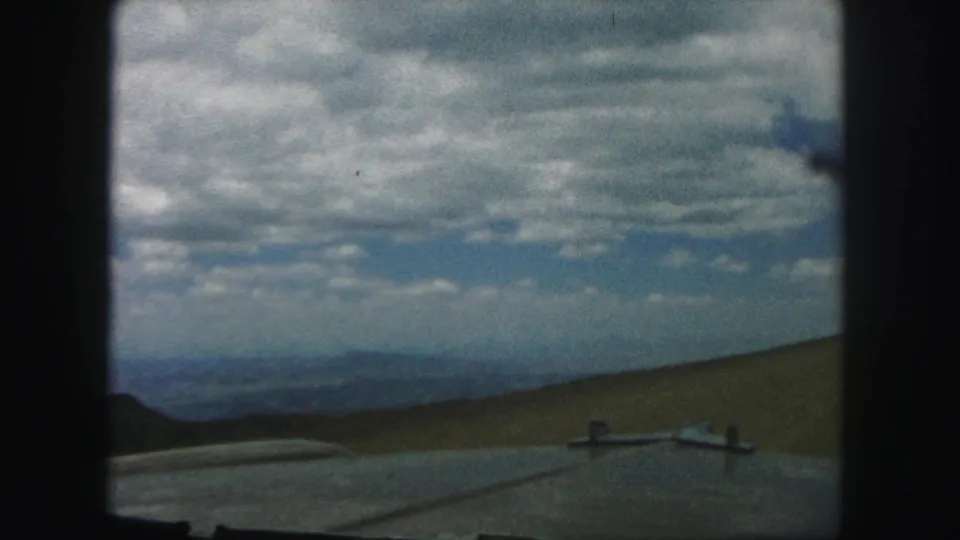 Colorado Springs-area 8mm frame with the car foreground, rounded hills, hazy distant ridges, and a large partly cloudy sky.