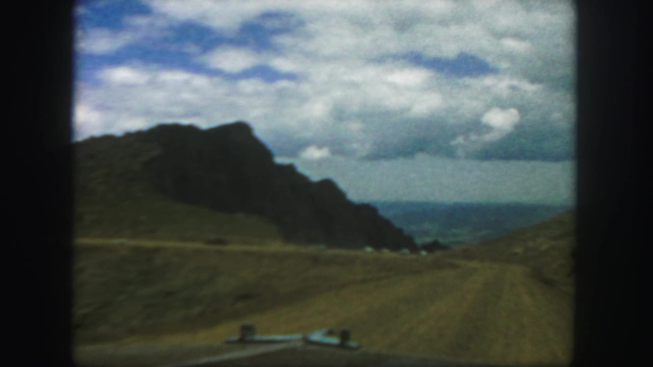 1958 Colorado 8mm frame showing a dirt road leading between rugged canyon slopes under a cloudy sky.
