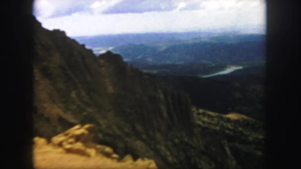 1958 Colorado 8mm frame looking past a steep rocky canyon wall toward a distant valley and winding river.