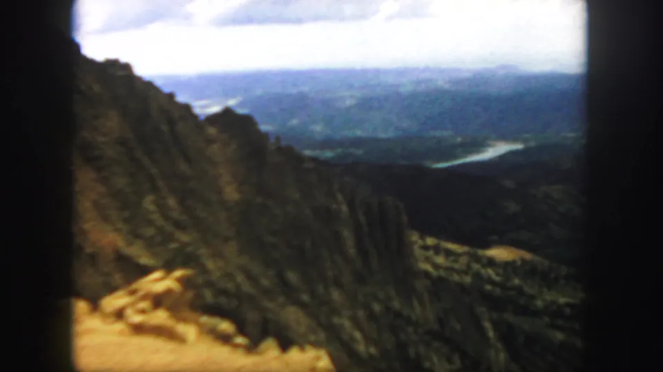 1958 Colorado home-movie frame of a steep canyon slope and pale roadside edge above a distant river valley.