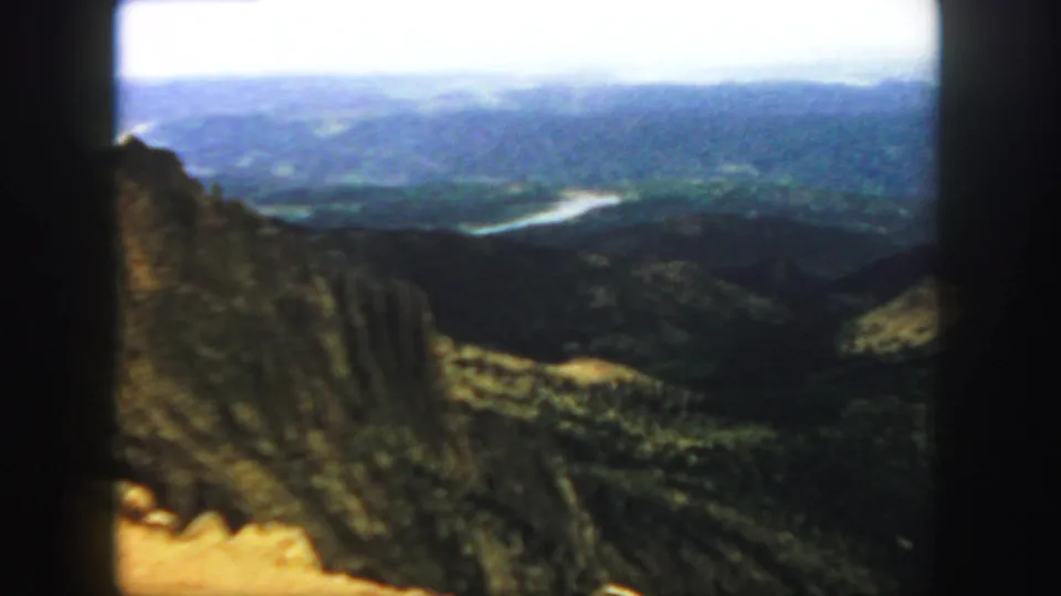 1958 Colorado 8mm frame showing a soft, grainy mountain overlook with a cliff face at left and a river crossing the valley below.
