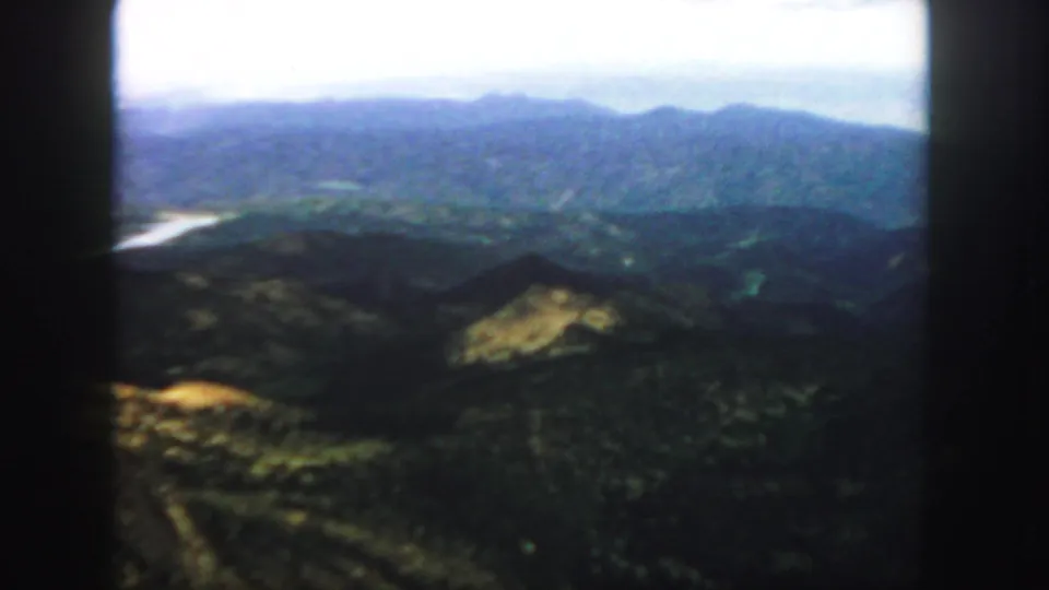 1958 Colorado frame with distant ridgelines, wooded valley terrain, a pale waterway, and soft color typical of scanned 8mm film.