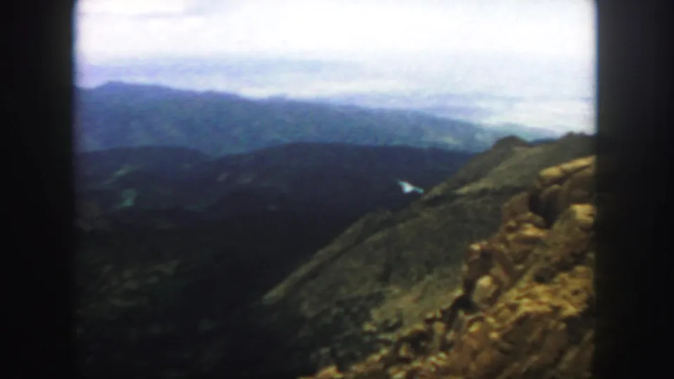 High Colorado trail view with rocky foreground, distant ridges, and a small pale water shape or valley feature below.