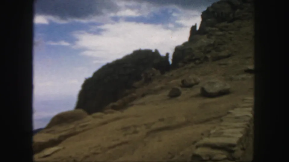 1958 Colorado home-movie view of a rugged hillside, boulders, and a pale cloudy sky in soft 8mm color.