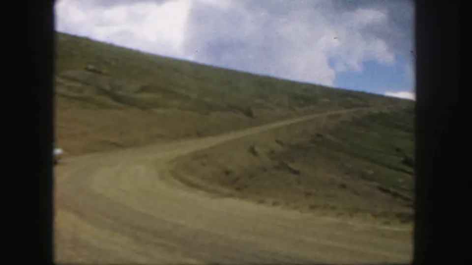 The final frame holds on a winding dirt road through an arid Colorado mountain landscape in soft 8mm color.
