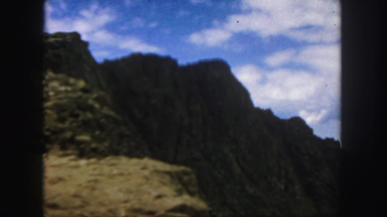 1958 Colorado home-movie frame showing rocky arid mountain slopes viewed from inside a moving vehicle.