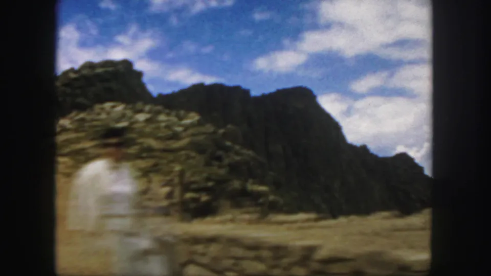 Motion-softened 1958 Colorado home-movie frame of rocky arid terrain seen through a car window.