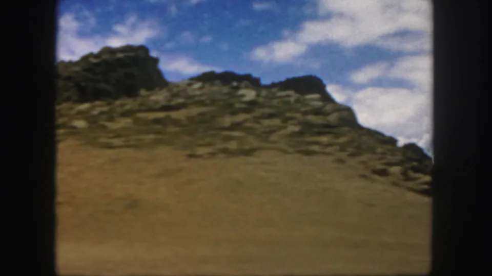 End frame from a 1958 Colorado 8mm travel clip showing dry ground and a rocky ridge from inside a vehicle.