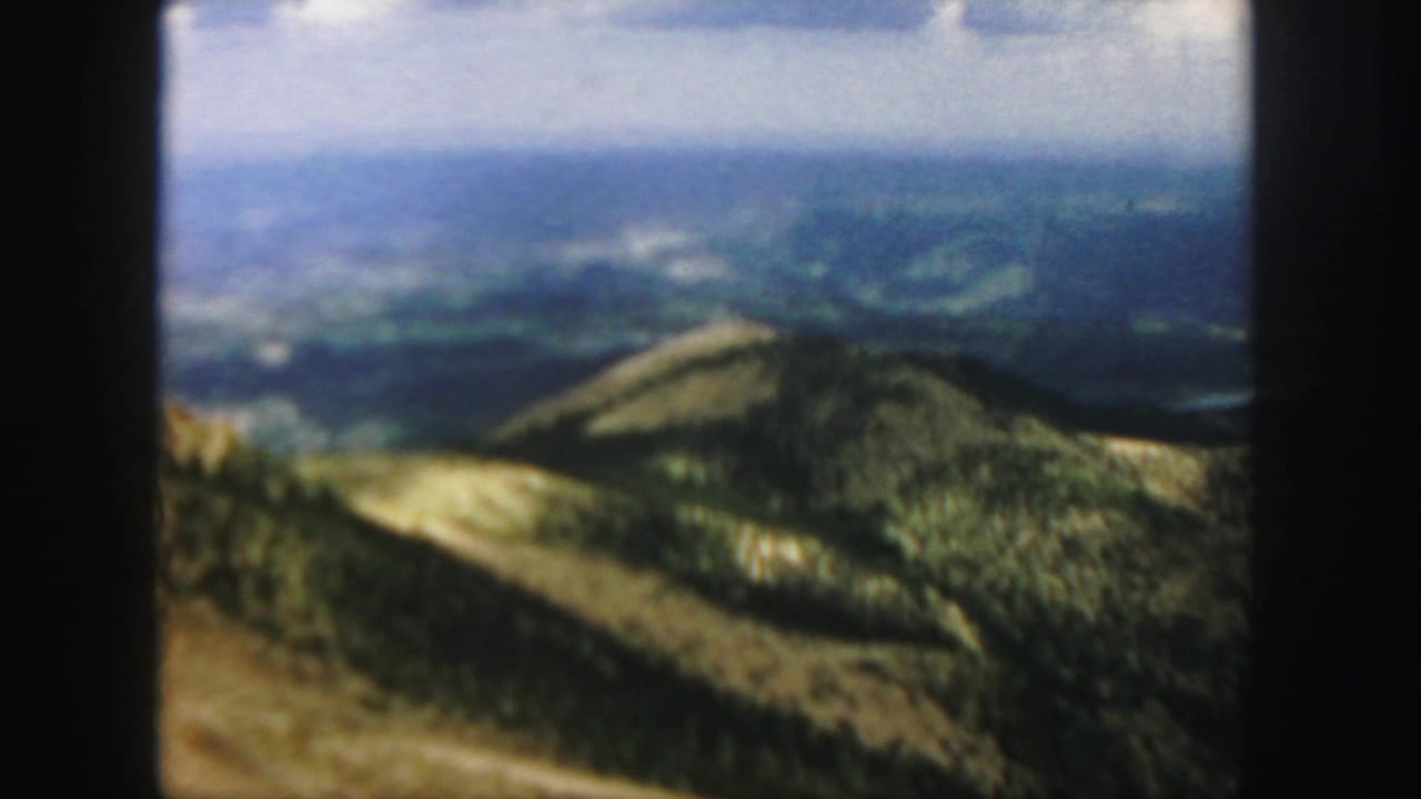 Forested mountain ridge and distant hazy ranges under clouds.
