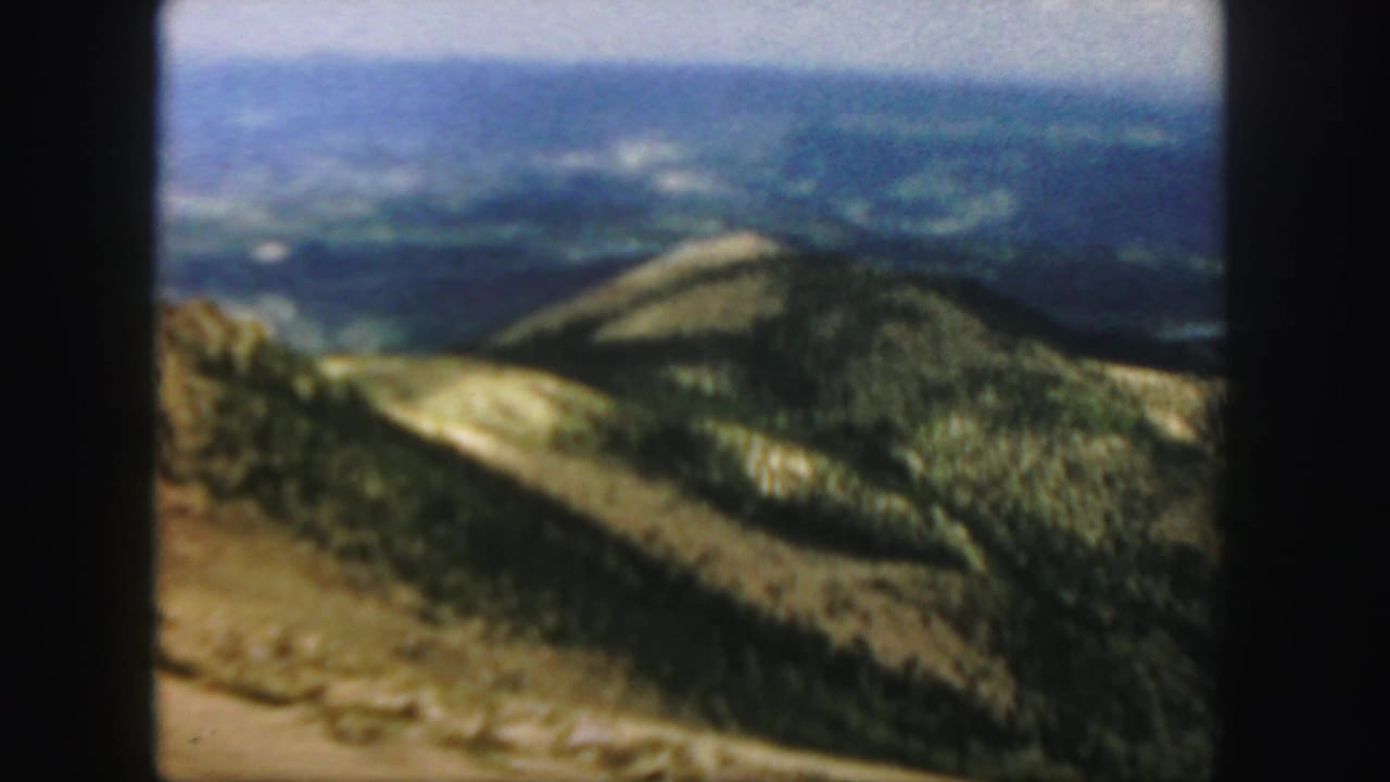 Soft 8mm view of mountain ridges and a pale road across open slopes.