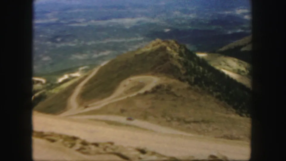 Colorado 1958 8mm view across a mountain road, tan hillside, scattered trees, and a broad valley in the distance.