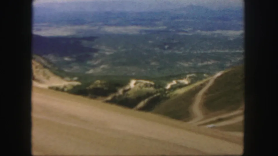 1958 Colorado home-movie view of dusty road bends across steep mountain terrain and a broad valley backdrop.