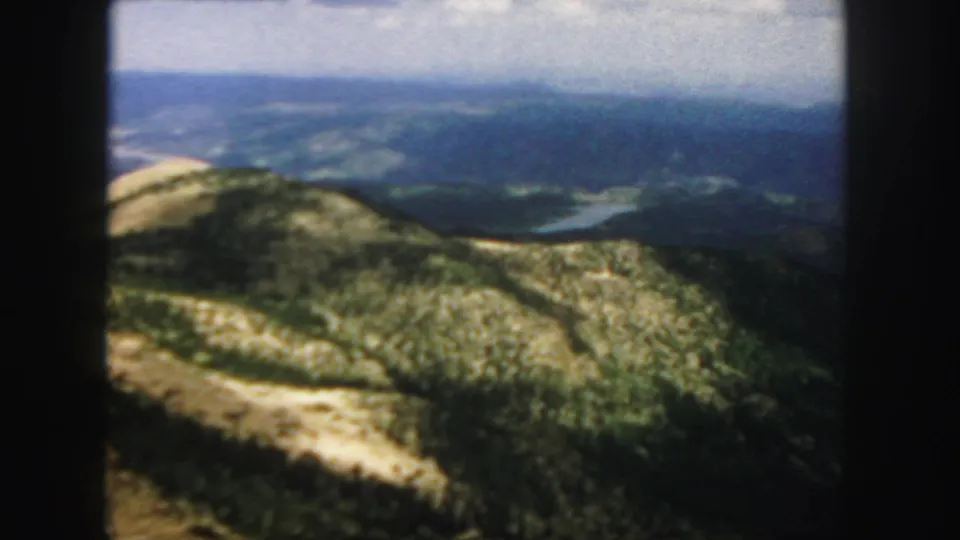 1958 Colorado 8mm view of a sunlit ridge dropping toward distant blue-green valley terrain.