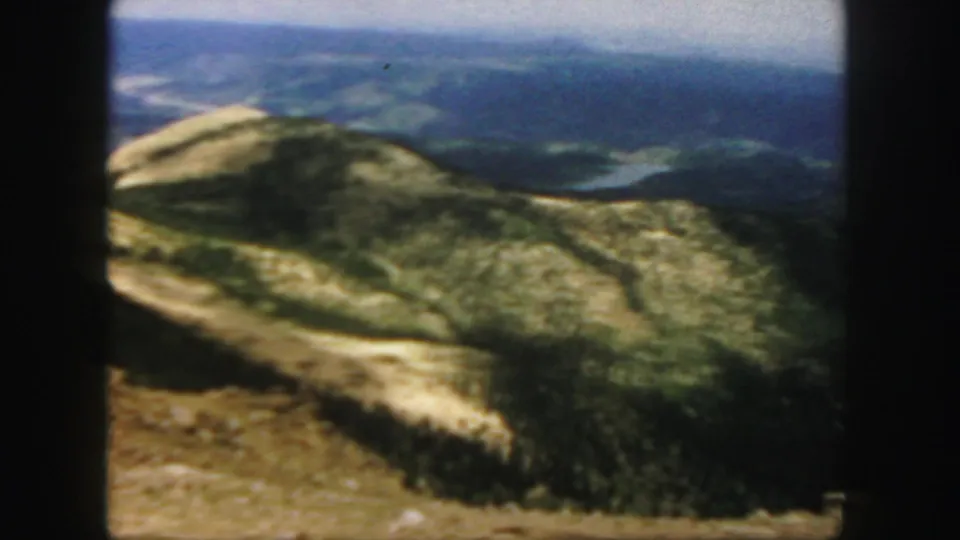 1958 Colorado home-movie view of a high mountain ridge, distant lake, and layered blue hills under haze.