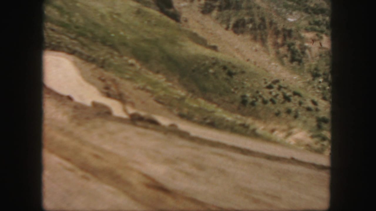 1958 Colorado 8mm frame showing a pale road or wash below dry hillsides, with dark film-gate borders around the view.