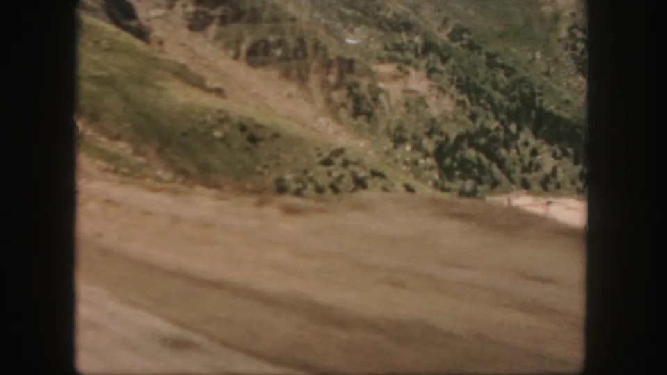 Colorado home-movie frame from 1958 showing dry hillside terrain and a pale roadside area, divided by dark 8mm frame borders.