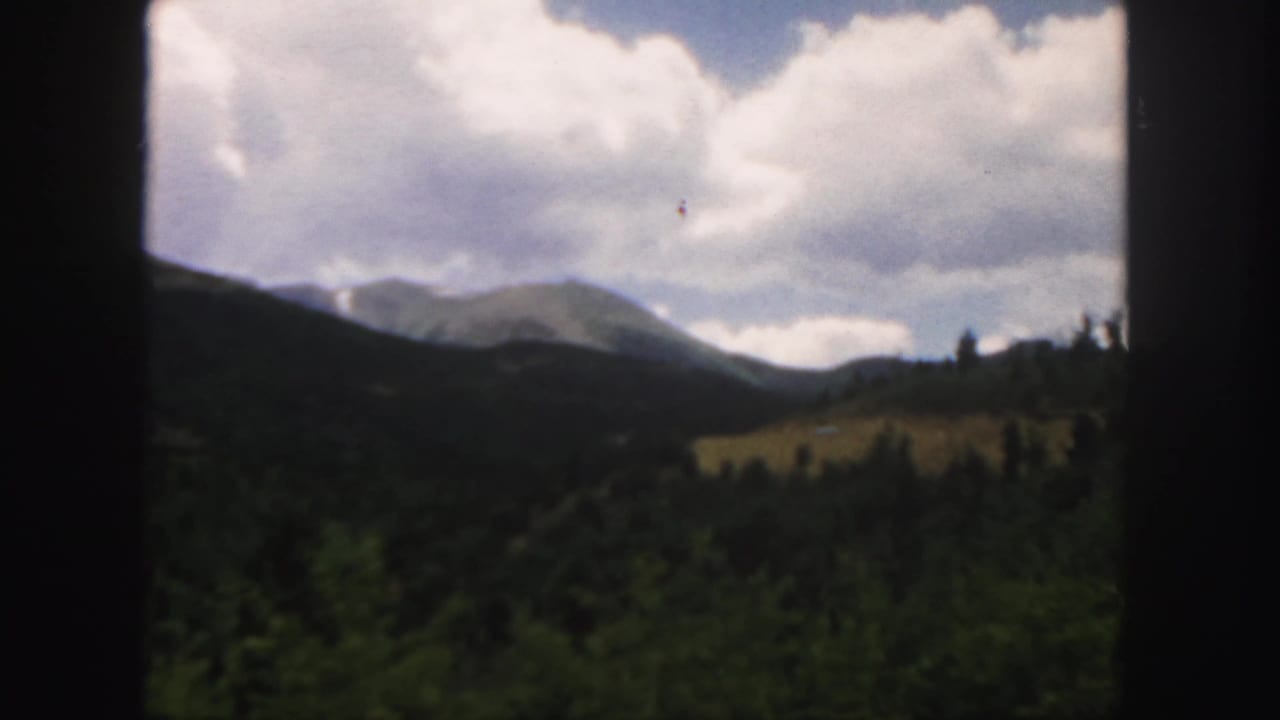 Mountain ridge under large clouds with dark forested slopes in the foreground.