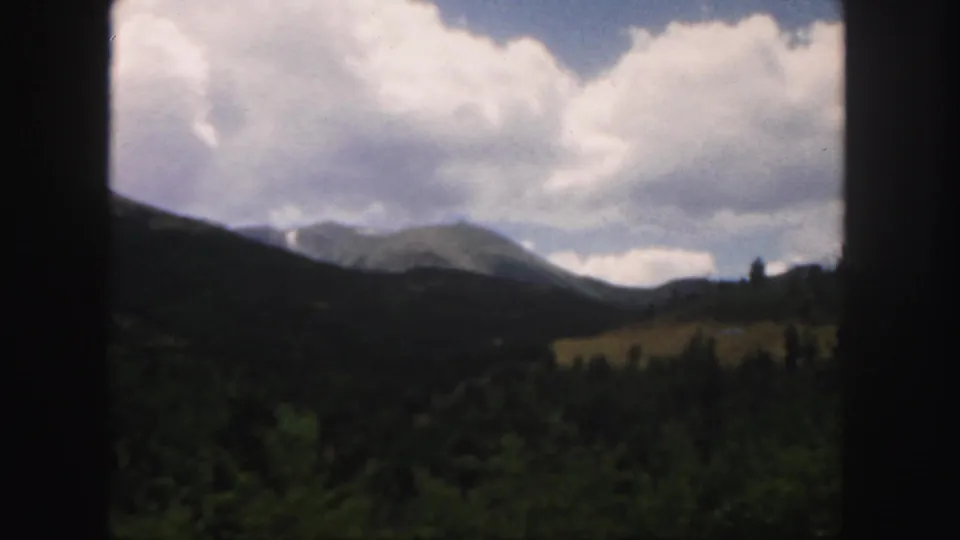 A second 1958 Colorado 8mm view of mountains, forest, and a small pale clearing beneath heavy clouds.