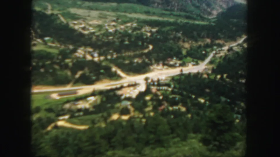 1958 Colorado 8mm aerial-style view of a small valley settlement with roads, buildings, trees, and surrounding hills.