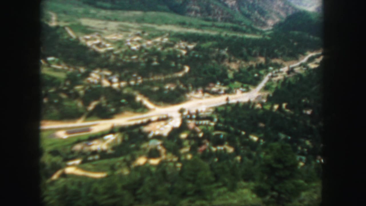 Aerial view of a green mountain valley with winding roads and scattered buildings.