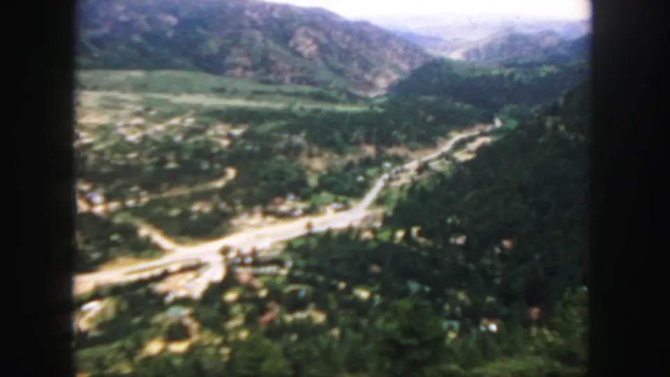 A 1958 Colorado 8mm frame shows a wooded valley, winding road network, scattered structures, and mountains beyond.