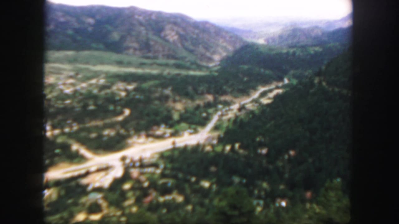 Forested mountain valley with a winding road and distant ridges seen from above.