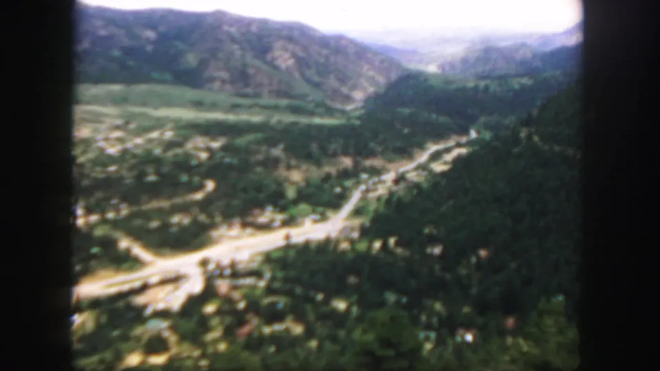 1958 Colorado 8mm frame showing a high view over a forested mountain valley, winding road, and hazy distant ridges.