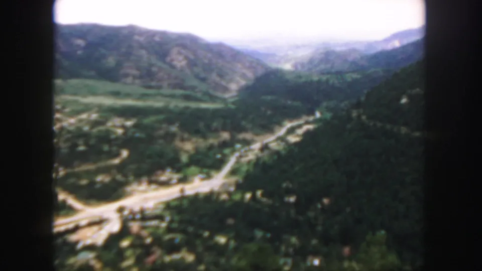 1958 Colorado home-movie view of a mountain valley, with roads cutting through dark trees and ridges fading into the distance.