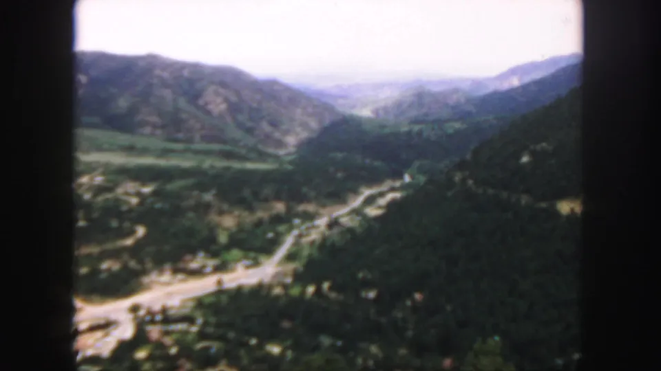 1958 Colorado 8mm frame looking across a green valley, with a pale road below and mountain slopes on both sides.