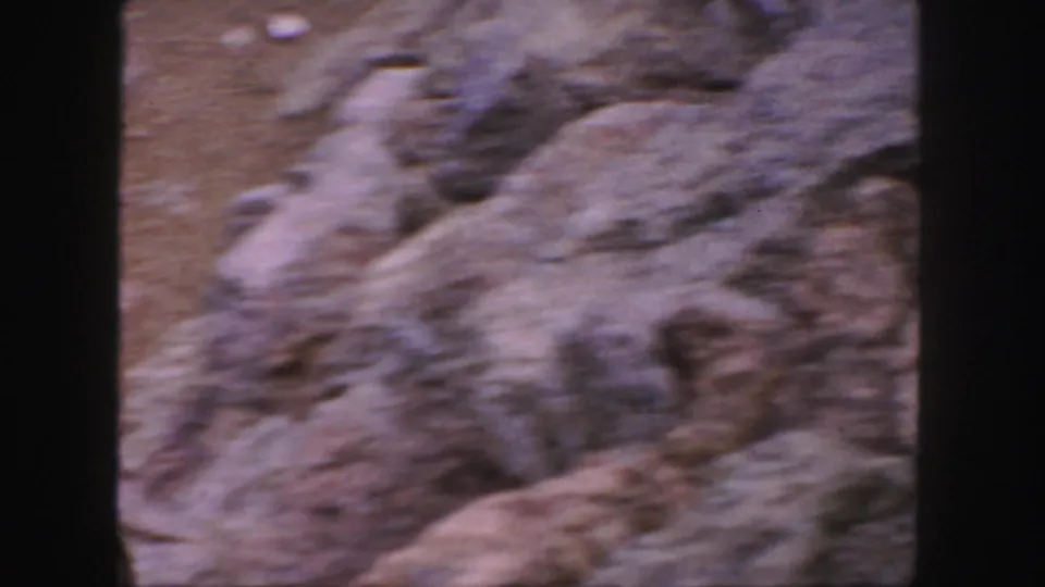 The frame shows soft, handheld rocky terrain from the Colorado home-movie clip, with motion blur and no clear people or signage.
