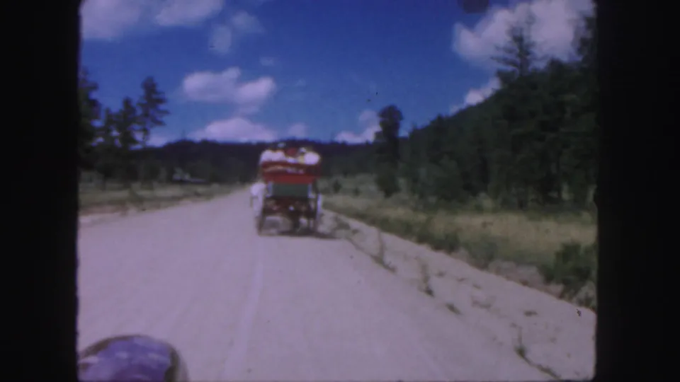 The horse-drawn cart appears farther down the Colorado dirt road, framed by forested hills and scattered clouds.