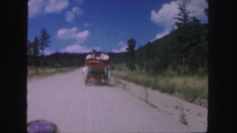 Soft 8mm frame of a horse-drawn cart traveling away on a rural Colorado road, with passengers visible only at a distance.