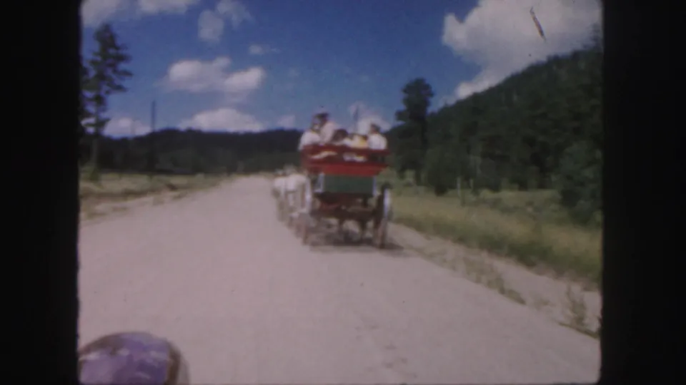 1958 Colorado 8mm frame showing a red and green carriage with passengers moving away along a sunlit dirt road.