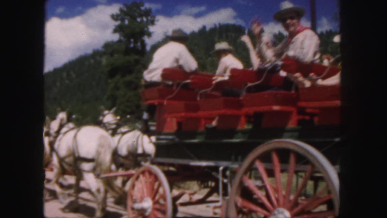 1958 Colorado 8mm frame showing passengers in a red carriage behind white horses with wooded hills in the background.