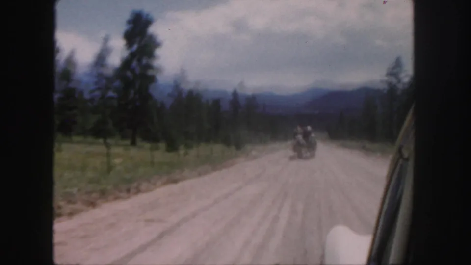 1958 Colorado 8mm view from a car following a horse-drawn carriage down a dusty road through pine country.